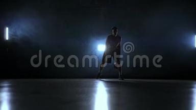 技能运球篮球运动员在黑暗的篮球场与背光背在烟雾。 慢动作